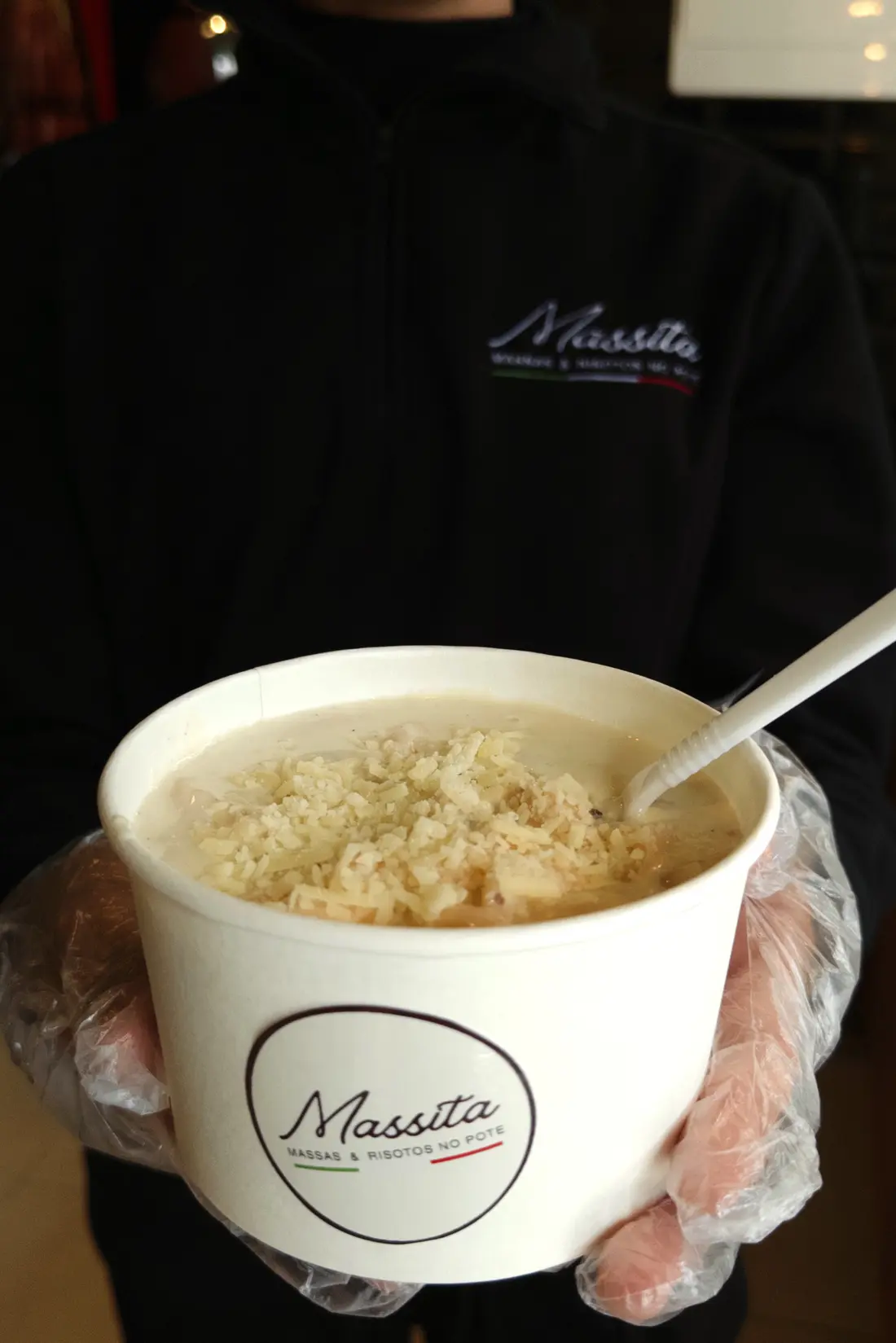 Atendente da Massita entregando um pote de risoto coberto com queijo parmesão ralado na hora